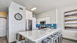 A modern kitchen with a central island, stainless steel appliances, and a blue backsplash. - Shores of Panama 2003 - Renovated 2 bedroom, with Bunkroom with a Reserved Parking Space! 2 Condo by RedAwning (Panama City Beach)