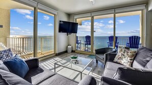 A balcony with a view of the ocean, a ceiling fan, a flat-screen TV, and outdoor seating with blue chairs. - Shores of Panama 2003 - Renovated 2 bedroom, with Bunkroom with a Reserved Parking Space! 2 Condo by RedAwning (Panama City Beach)