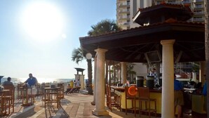 An outdoor dining area with tables and chairs, a bar, and a view of the sea. - Shores Of Panama 318 - Nice 2bd, Sleeps 8! Great View! Reserved 3rd Floor Parking Space! 2 Bedroom Condo by RedAwning (Panama City Beach)