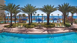A pool area with palm trees, lounge chairs, and umbrellas. - Shores Of Panama 318 - Nice 2bd, Sleeps 8! Great View! Reserved 3rd Floor Parking Space! 2 Bedroom Condo by RedAwning (Panama City Beach)