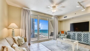 A spacious living room with a balcony, a flat-screen TV, and a ceiling fan. - Shores of Panama 808- 1 Bedroom+Bunk Room, Free Fun! Updated! Sleeps 6. 1 Condo by RedAwning (Panama City Beach)