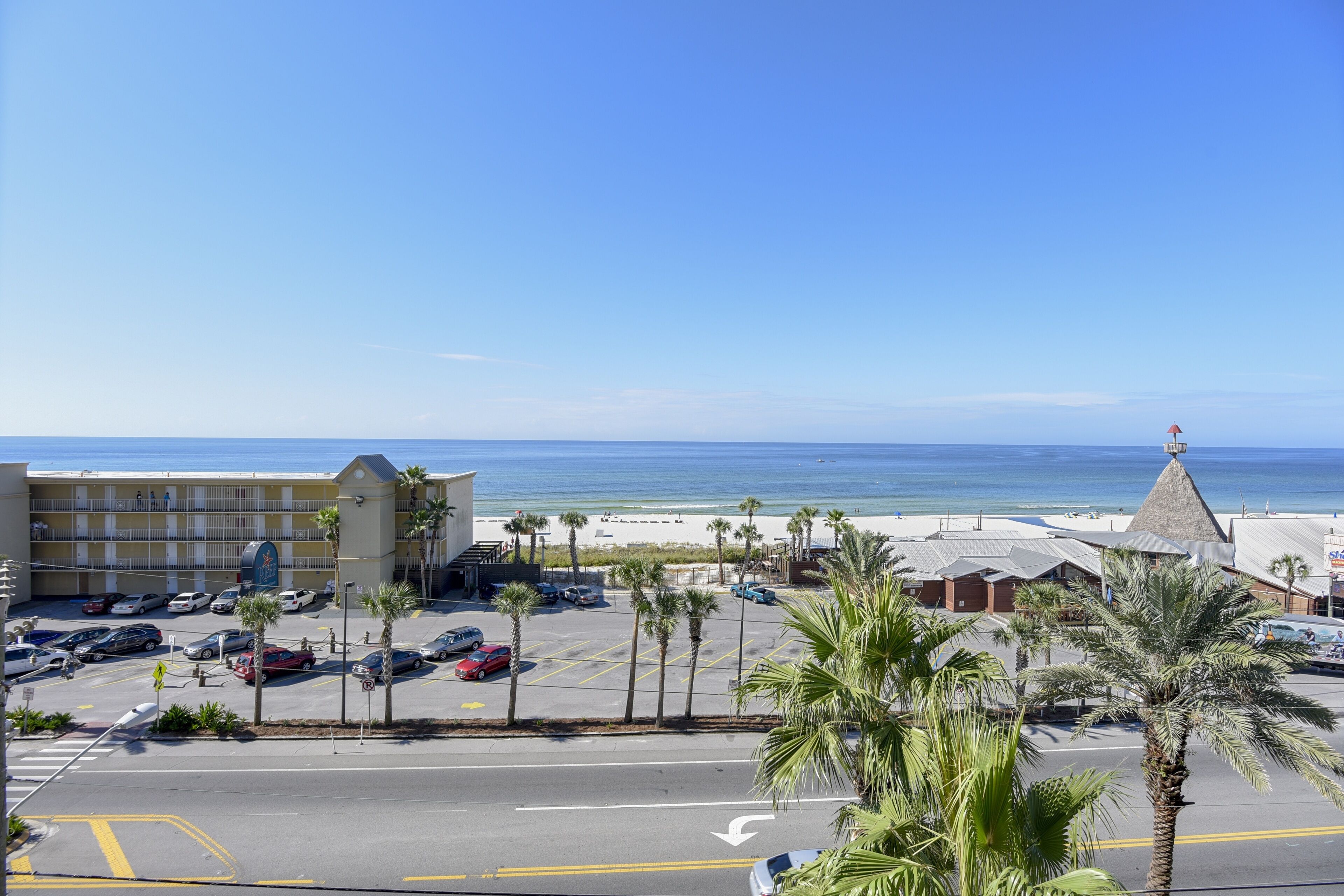 Un hotel con aparcamiento, vistas a la playa y palmeras.