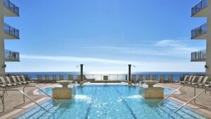 A swimming pool with a view of the ocean, surrounded by lounge chairs and a tiled deck. - Origin 1038, Sunset & Gulf View! Perfect For 2! Free Fun! 1 Bedroom Condo by RedAwning (Panama City Beach)