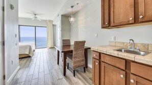 A kitchen with wooden cabinets, a countertop sink, and a dining area with a table and chairs. - Origin 1038, Sunset & Gulf View! Perfect For 2! Free Fun! 1 Bedroom Condo by RedAwning (Panama City Beach)