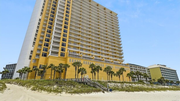 Un hotel moderno de gran altura con varios balcones, situado cerca de una playa con palmeras.