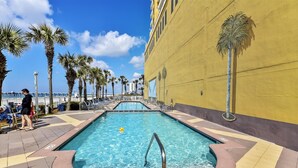 Un área de piscina con agua azul cristalina, rodeada de palmeras y un edificio amarillo.