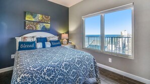 A bedroom with a bed, a nightstand, a window with a city view, and decorative wall art.