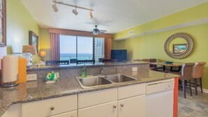 A kitchen with granite countertops, a sink, and a dining area with a table and chairs. - Shores Of Panama 621-sleeps 8, Free Beach Fun! Reserved Parking Space! 2 Bedroom Condo by RedAwning (Panama City Beach)