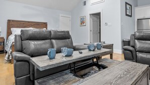 A modern living room with a leather sofa, a wooden coffee table, and a dining table with blue bowls and a wine glass. - Appian Way Maltese Cottage 1 Bedroom Cabin by RedAwning (Fredericksburg)