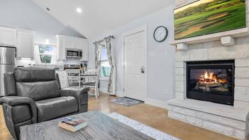 A modern living room with a fireplace, leather sofa, dining area, kitchen, and a large flat-screen TV.