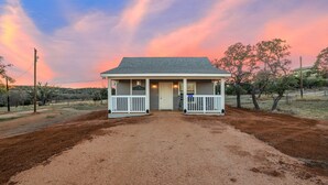 A two-story building with a porch, a sign reading "MALTSEY," and a dirt driveway leading to it. - Appian Way Maltese Cottage 1 Bedroom Cabin by RedAwning (Fredericksburg)