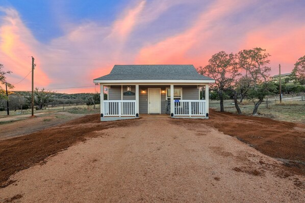 A two-story building with a porch, a sign reading "MALTSEY," and a dirt driveway leading to it. - Appian Way Maltese Cottage 1 Bedroom Cabin by RedAwning (Fredericksburg)