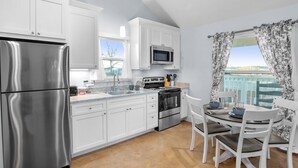 A modern kitchen with white cabinetry, stainless steel appliances, and a dining area with a table and chairs. - Appian Way Maltese Cottage 1 Bedroom Cabin by RedAwning (Fredericksburg)