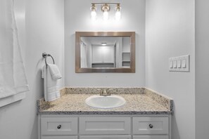 A bathroom with a granite countertop sink, a mirror with a gold frame, and a towel rack. - Appian Way Maltese Cottage 1 Bedroom Cabin by RedAwning (Fredericksburg)