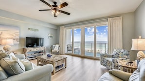 A spacious living room with a large TV, comfortable seating, a ceiling fan, and a balcony with a view of the ocean. - Laketown Wharf 1003, Gulf View, Sleeps 6. Free Fun! Updated! 1 Bedroom Condo by RedAwning (Panama City Beach)