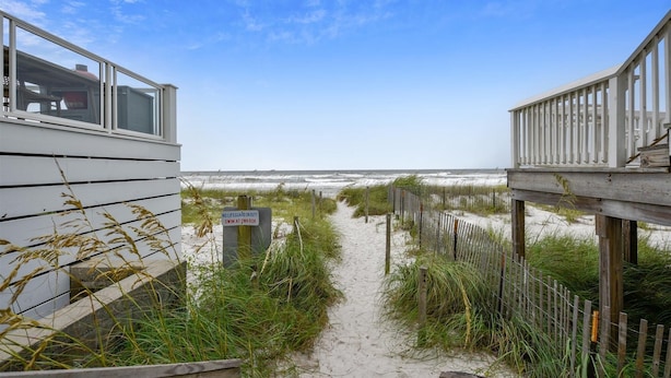Un sentier menant à la plage et aboutissant à une structure en bois sur laquelle est affiché un panneau indiquant la présence d’un sauveteur.