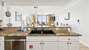 A modern kitchen with granite countertops, white cabinetry, and a stainless steel dishwasher. - Emerald Beach 1830 - 2 Bedroom/2 Bath+Bunks 2 Condo by RedAwning (Panama City Beach)