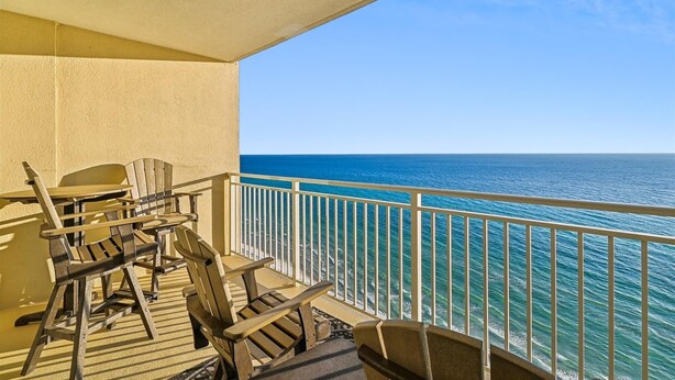 A balcony with a view of the ocean, featuring wooden chairs and a table. - Emerald Beach 1830 - 2 Bedroom/2 Bath+Bunks 2 Condo by RedAwning (Panama City Beach)