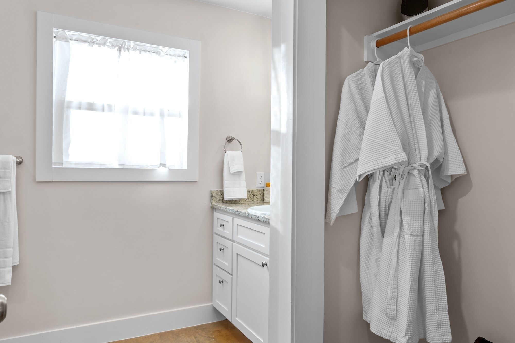 A bathroom with a window, a towel rack, a sink, and a robe hanging on a rack.