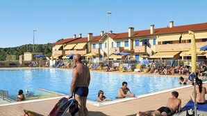 Un espace autour d’une piscine où des personnes se prélassent au soleil et nagent, le tout entouré d’immeubles à plusieurs étages dotés de balcons.