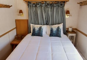 A neatly made bed with a white duvet and two pillows with a forest print, a wooden headboard, and two wall-mounted lamps. - Cozy chalet on the Swan River at Tiger Run (Breckenridge)