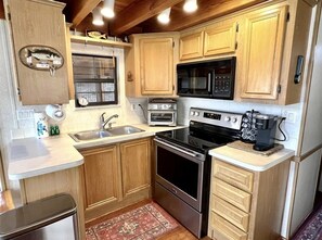 A compact kitchen with wooden cabinets, a microwave, a toaster, an oven, and a coffee maker. - Cozy chalet on the Swan River at Tiger Run (Breckenridge)