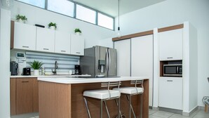 A modern kitchen with white cabinets, a stainless steel refrigerator, a built-in microwave, and a bar area with stools. - House close to the beach, adventure parks and authentic Puerto Rican restaurants (Luquillo)