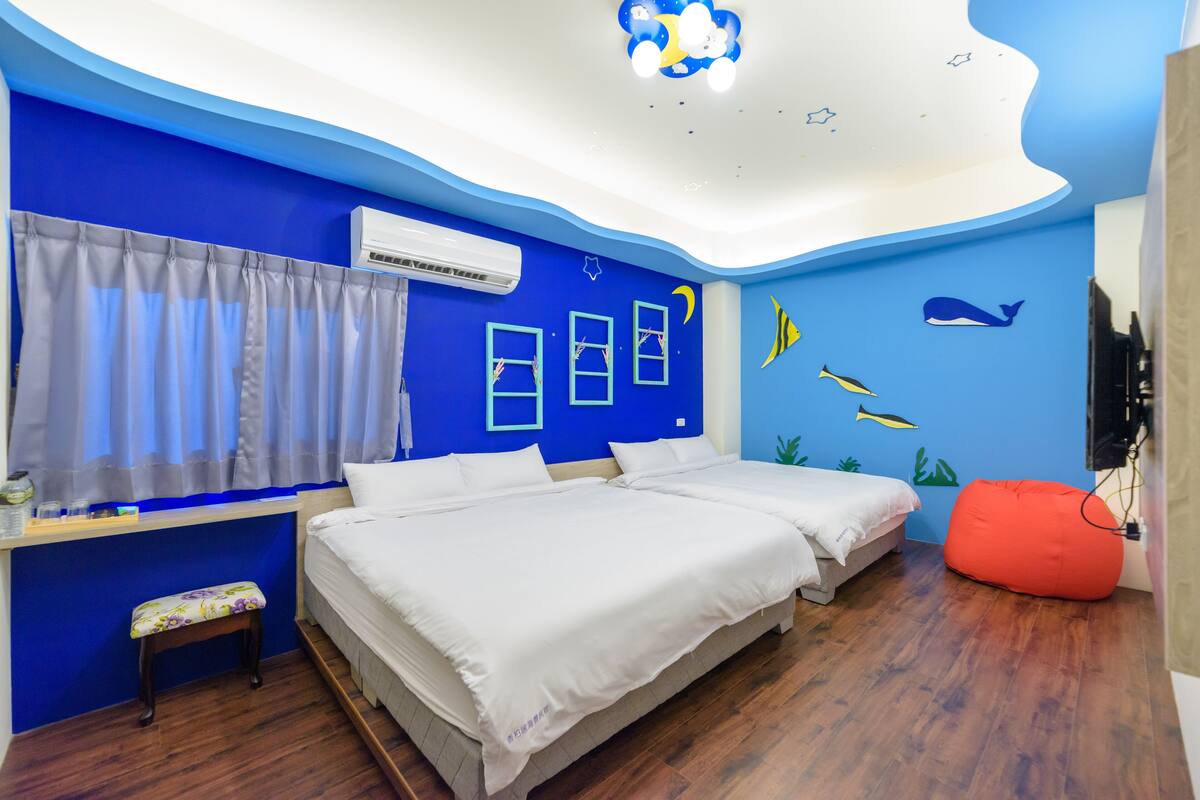 Quarto com duas camas, um banco, um assento de grãos vermelhos e uma parede decorada com vida marinha.