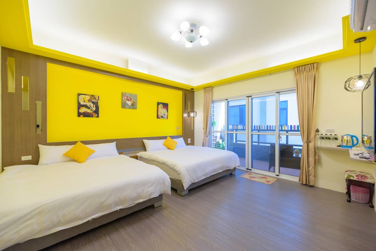 Quarto de hotel com duas camas, uma varanda e vista, e uma mesa pequena com comodidades.