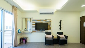 Un salon moderne avec un téléviseur à écran plat fixé au mur, deux fauteuils en osier noir avec des coussins, une petite table et une fenêtre avec des rideaux.