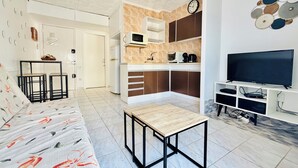 Ett modernt vardagsrum med en soffa, ett soffbord, en tv och en köksdel med mikrovågsugn och kaffebryggare.