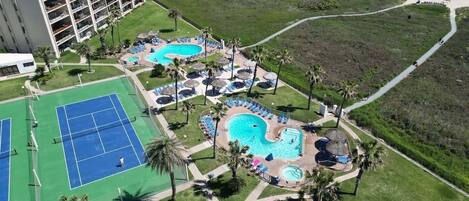 Vista aérea de un complejo turístico con múltiples piscinas, canchas de tenis y un gran edificio de hotel.