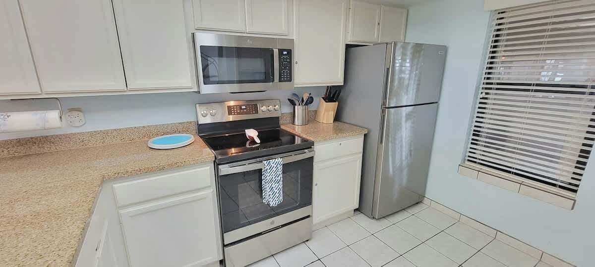 A modern kitchen with white cabinets, stainless steel appliances, a microwave, oven, and refrigerator.