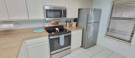 A modern kitchen with white cabinets, stainless steel appliances, a microwave, oven, and refrigerator.