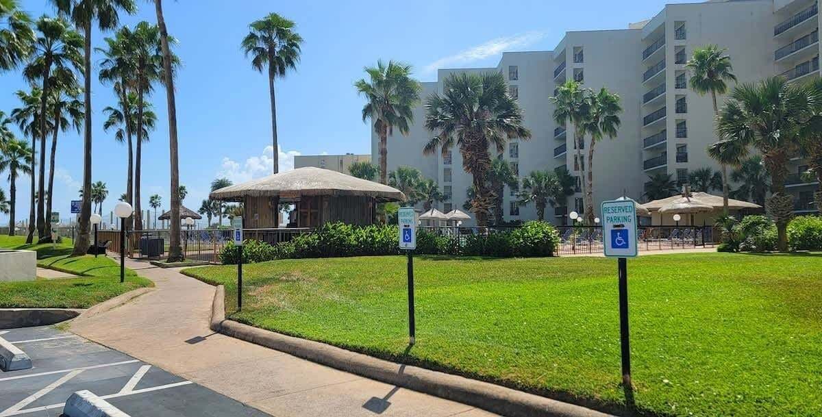 A hotel courtyard with palm trees, a thatched-roof structure, and a parking sign indicating reserved parking.