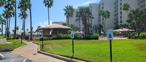 A hotel courtyard with palm trees, a thatched-roof structure, and a parking sign indicating reserved parking.