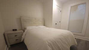 Un dormitorio con cama, mesita de noche, puerta y ventana con persianas.