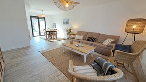 Un salon spacieux doté d’un plancher en bois, d’un canapé, d’une table basse, de fauteuils en osier et d’un coin repas avec une table et des chaises.