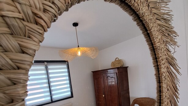 Une chambre à coucher avec un lit, une armoire en bois, une chaise en osier et une fenêtre avec des stores.