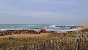Une plage bordée d’une clôture en bois, avec des affleurements rocheux et l’océan.