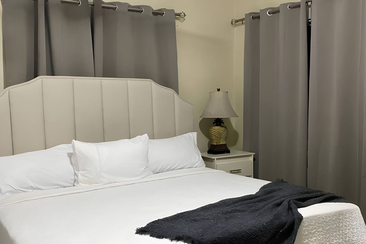 Une chambre d’hôtel avec un grand lit, une table de chevet avec une lampe et des rideaux gris.