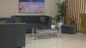 Un salon moderne avec un canapé gris, une table basse en verre, un ventilateur de plafond et un grand tableau représentant une scène de plage.