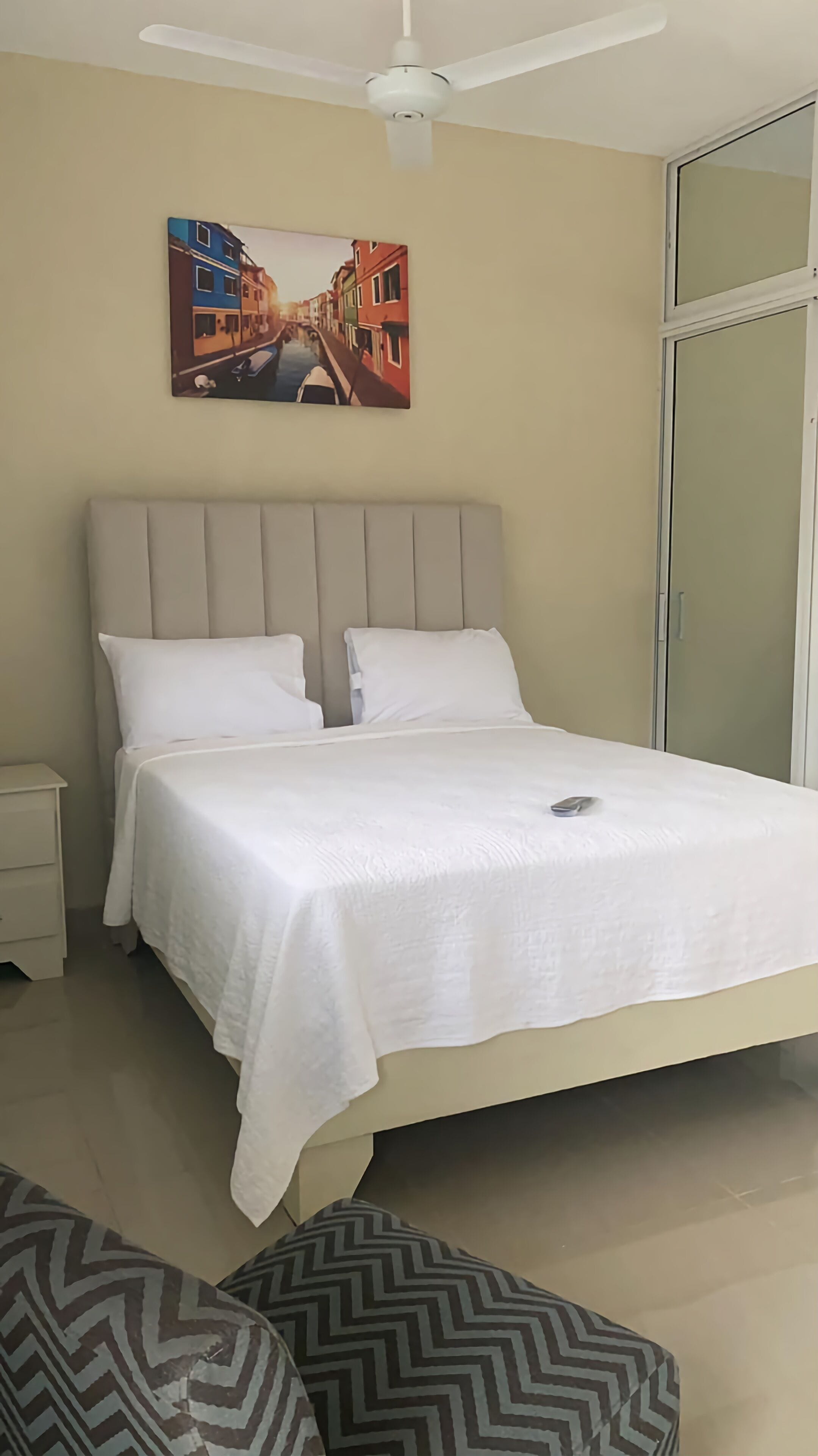 Una cama bien hecha con ropa blanca, un cabecero y una mesita de noche con cajón.