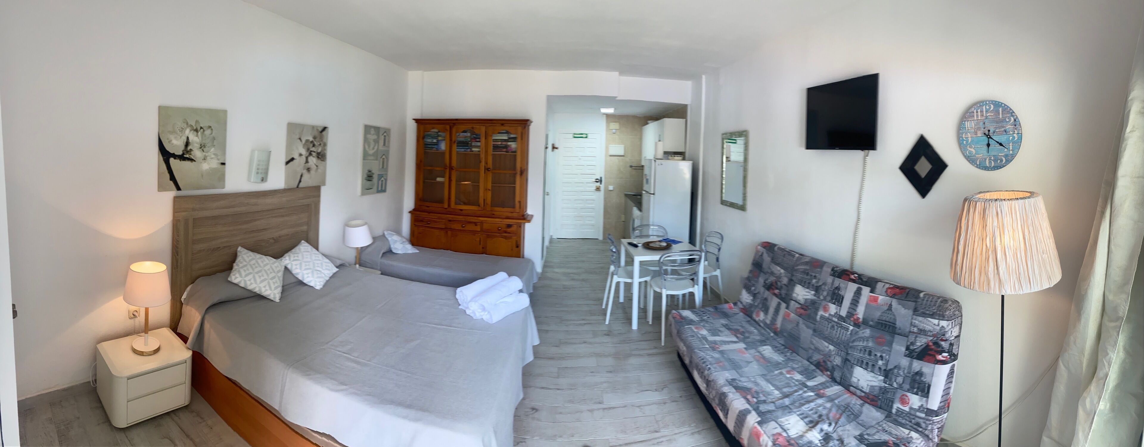 Ein Hotelzimmer mit Bett, Nachttisch, Lampe, Sofa, Fernseher und einer kleinen Essecke mit Stühlen und Tisch.
