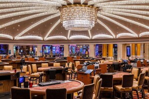 A spacious casino with multiple gaming tables and chairs, a large chandelier, and a variety of slot machines.