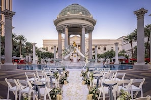 A wedding ceremony setup with a white aisle, floral decorations, and a central fountain. - 1-Bedroom Suite at a 4.5⭐️ Hotel (Las Vegas)