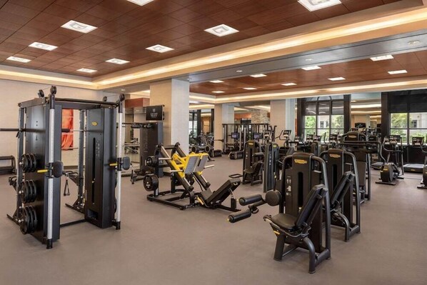 Une salle de sport équipée de divers appareils d’exercice, dotée de grandes fenêtres et d’un plafond en bois.