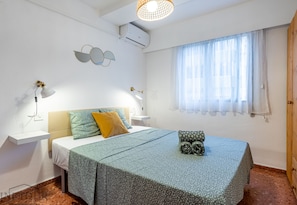 A bedroom with a bed, bedside tables, a window with curtains, an air conditioning unit, and wall decor.