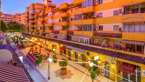 Un hotel de varios pisos con balcones, zonas de estar al aire libre y un patio con plantas en macetas.