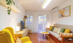 A living room with a sofa, yellow armchair, TV, and a small table with a lamp.
